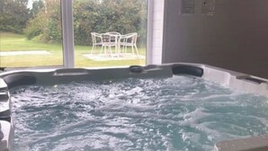 Ein Whirlpool mit sprudelndem Wasser, Blick auf eine Rasenfläche und Gartenmöbel, sowie ein Fenster.