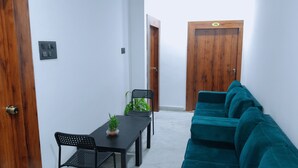A room with a teal sofa, a black dining table with chairs, a potted plant, and a wooden door with a number plate. - Hotel M Hyatt (Hyderabad)
