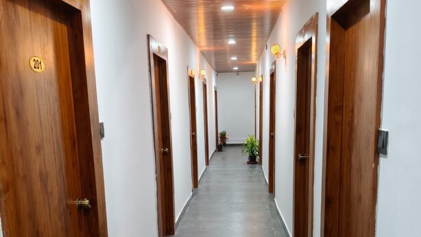 A long, narrow hallway with wooden doors on both sides, a tiled floor, and a ceiling with recessed lighting. - Hotel M Hyatt (Hyderabad)