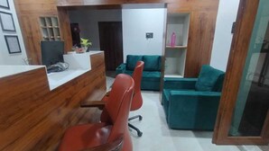 A reception area with a wooden reception desk, a red office chair, a teal sofa, and a glass partition. - Hotel M Hyatt (Hyderabad)