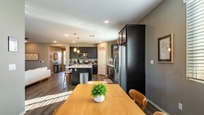A modern kitchen with dark cabinetry, a central island, and a dining area with a wooden table and chairs. - Luxe Indio Stay w/ Pool, Tiki Bar & Fire Pit Near Coachella | Longfellow (Indio)
