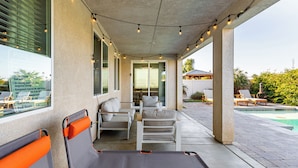 A covered outdoor seating area with chairs and a table, overlooking a swimming pool. - Luxe Indio Stay w/ Pool, Tiki Bar & Fire Pit Near Coachella | Longfellow (Indio)