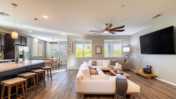 A spacious living area with a large sofa, wooden bar stools, a kitchen area, and a ceiling fan.