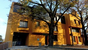 Un edificio amarillo con una escalera que conduce a la entrada, rodeado de árboles.