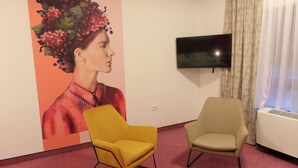 Una habitación con dos sillas, un televisor en la pared y un cartel grande.