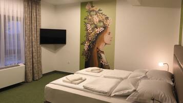 A hotel room with a bed, pillows, a flat-screen TV, a wall mural, and a window with curtains.