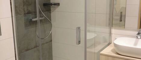Un baño moderno con ducha acristalada, lavamanos blanco y tocador de madera.