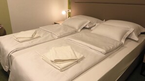 Una cama individual bien hecha con sábanas y almohadas blancas, una lámpara de noche y una pared con estampado floral.