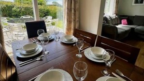 A dining area with a table set for four, a view of the outdoors, and a living area with a sofa and a window. - Primrose at Moorhead Country Holidays near Clovelly North Devon (Bideford)