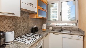 Uma cozinha compacta com bancadas de granito, fogão a gás, cafeteira e janela com vista para edifícios.