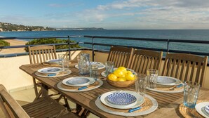 Mesa posta para refeição, com vista para o mar e uma linha de costa distante.