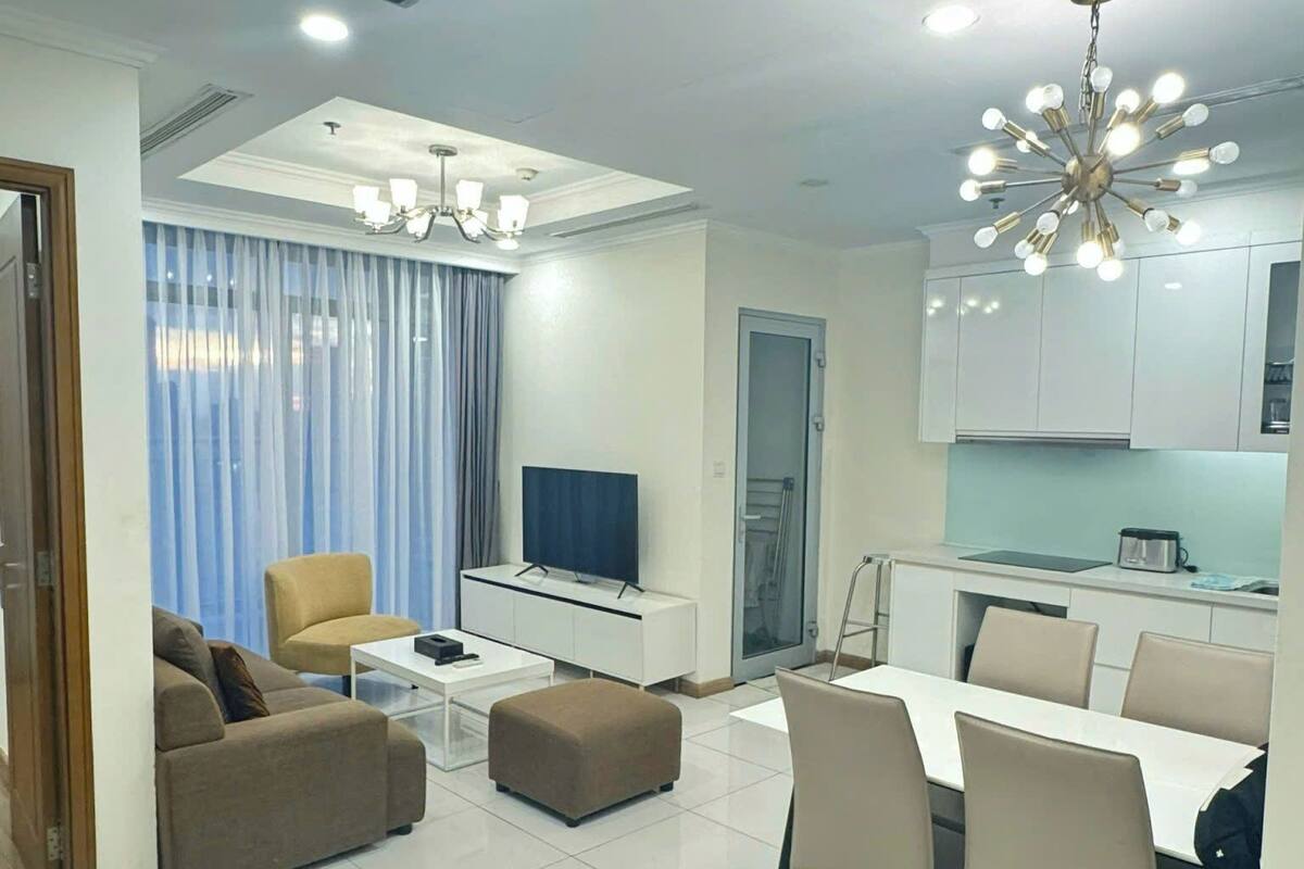 A modern living room with a sofa, ottoman, TV, and dining area.