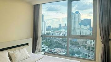 Ein Hotelzimmer mit einem großen Bett, Blick auf eine Stadtkulisse durch ein großes Fenster und einer an der Decke befestigten Klimaanlage.