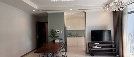 A modern living room with a dining area, a kitchen in the background, and a large window with curtains.