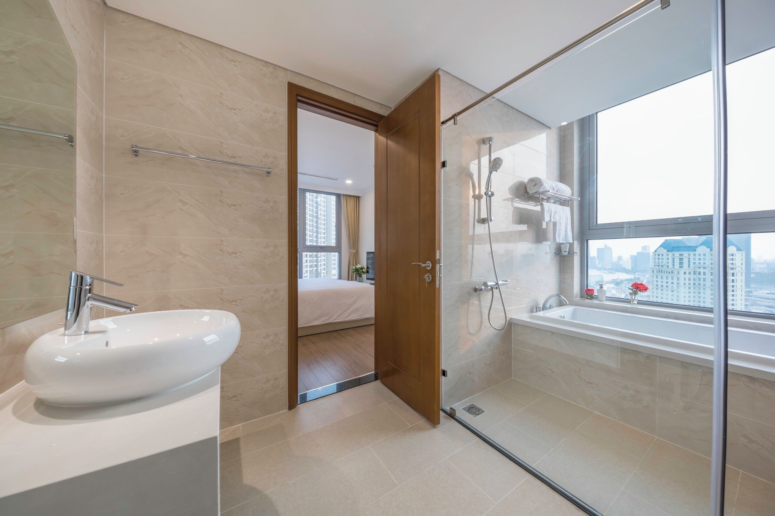 Un baño moderno con un lavabo grande, cabina de ducha con paredes de vidrio y una bañera con vista a la ciudad.