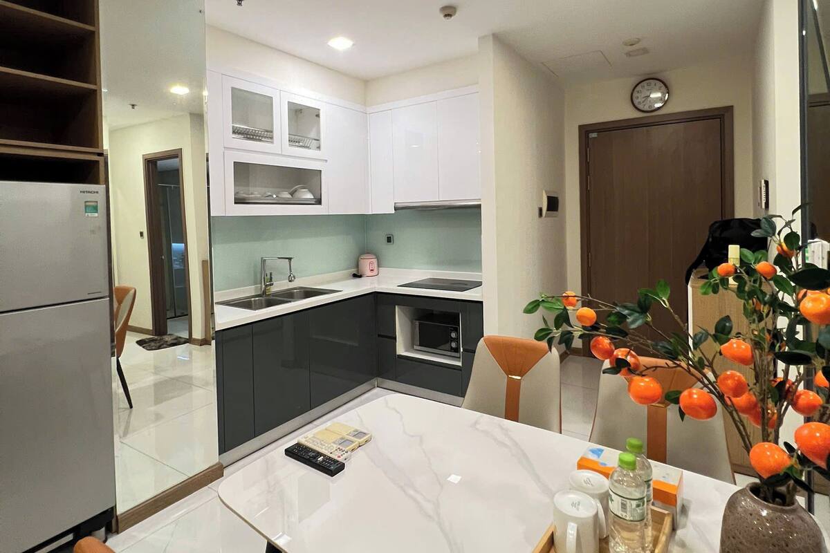 A modern kitchen with white cabinets, a microwave, and a sink. There is a dining table with chairs and a vase of oranges.