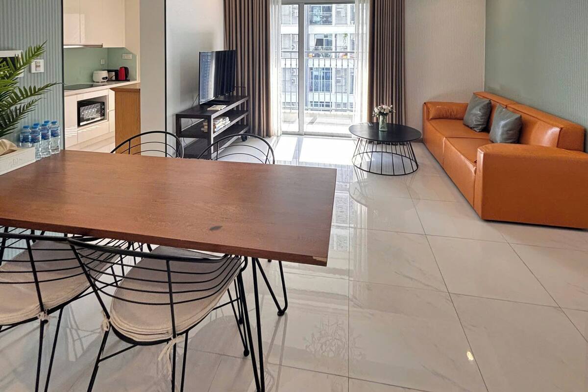 A modern living room with a sofa, a dining table with chairs, a TV, and a kitchen area in the background.