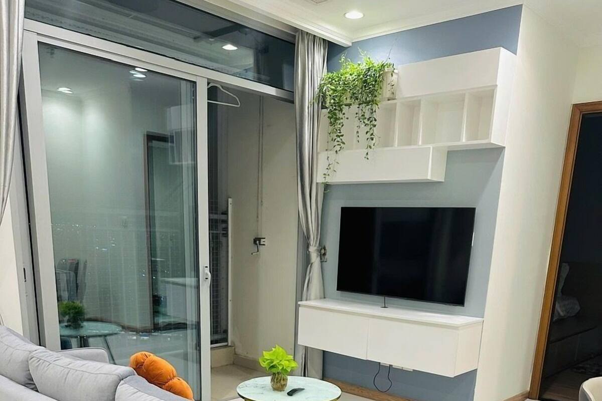 A modern living room with a grey sofa, a small round table with a plant, and a TV mounted on a white wall.