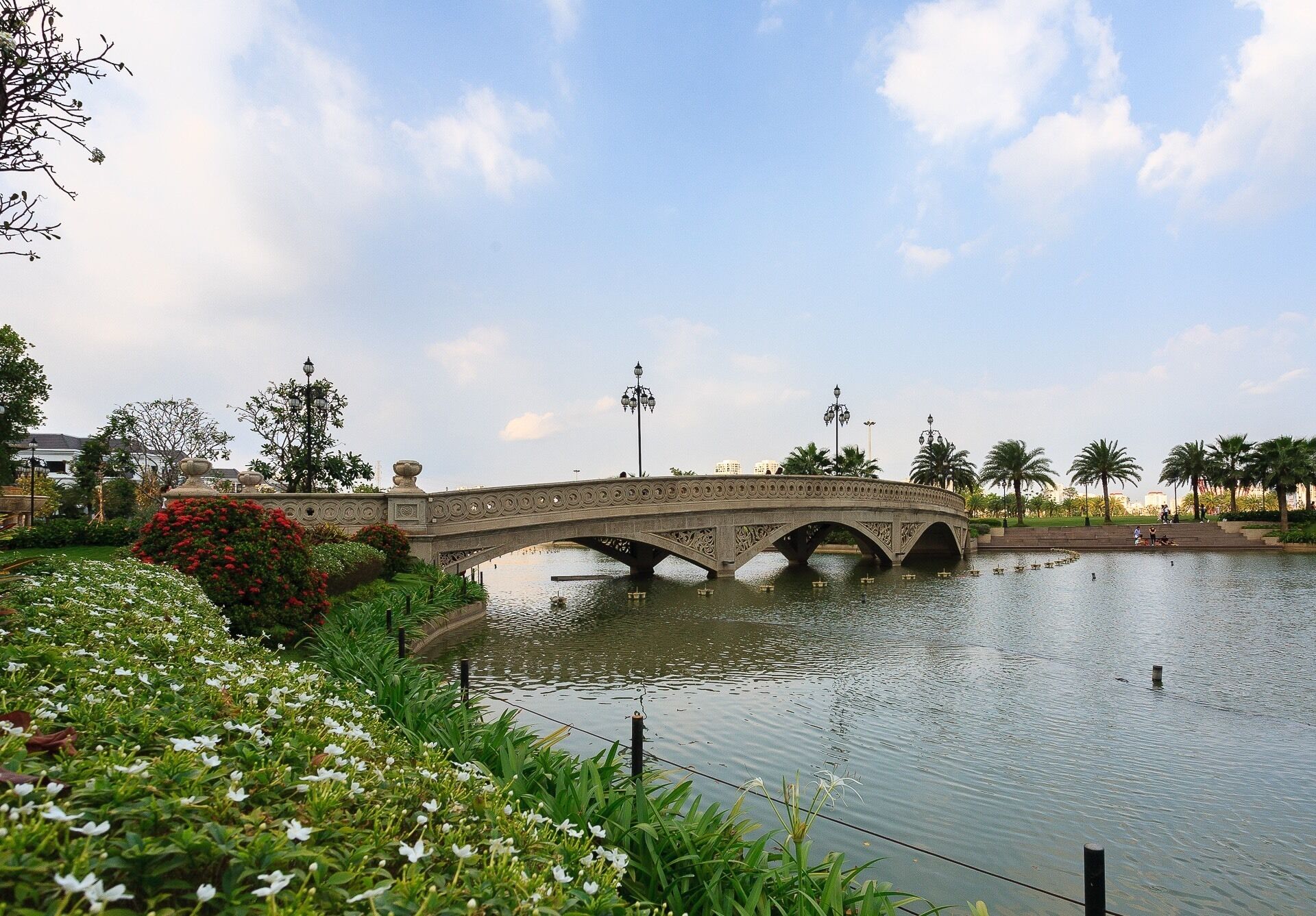 Un pont de pierre enjambant une étendue d’eau paisible, entouré d’une végétation luxuriante et de palmiers.