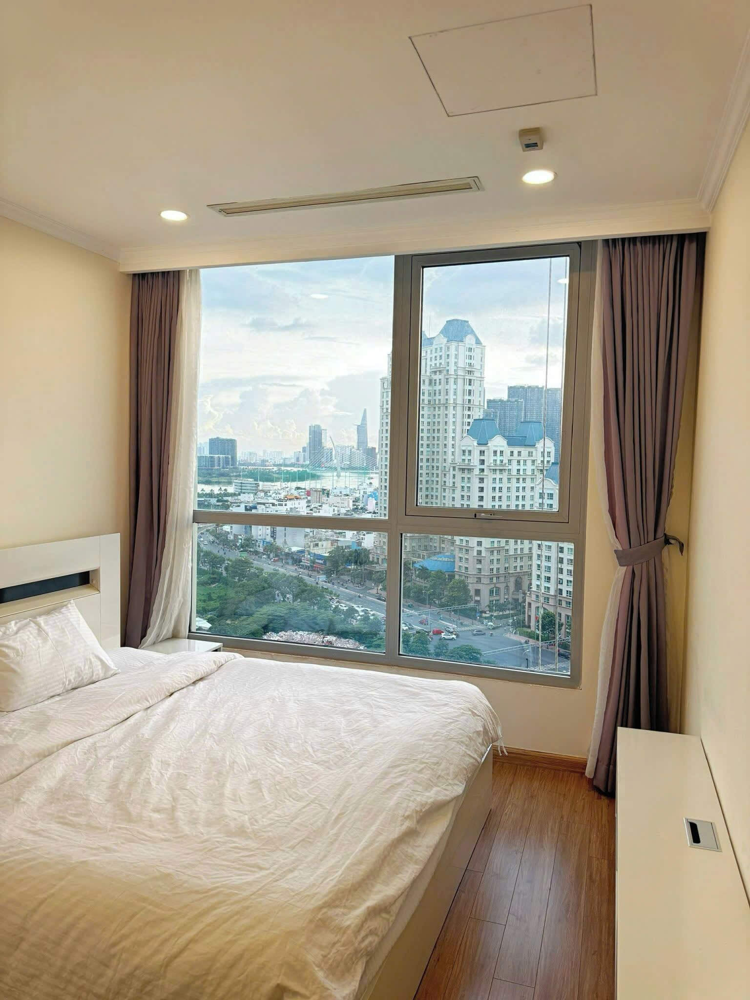 A hotel room with a large window, a bed, a bedside table, and a ceiling light.