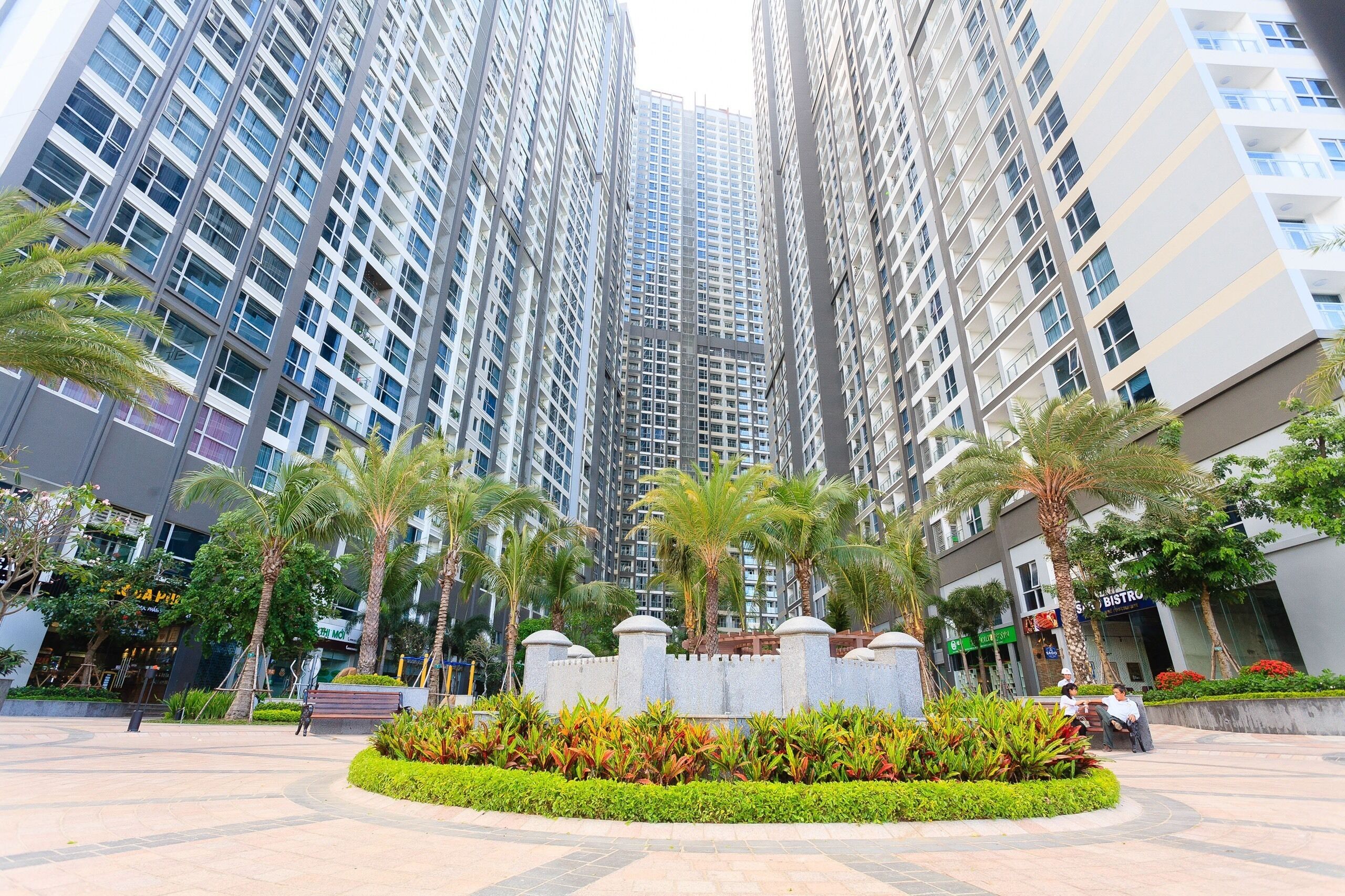 A modern high-rise building with a central courtyard featuring palm trees and a fountain.