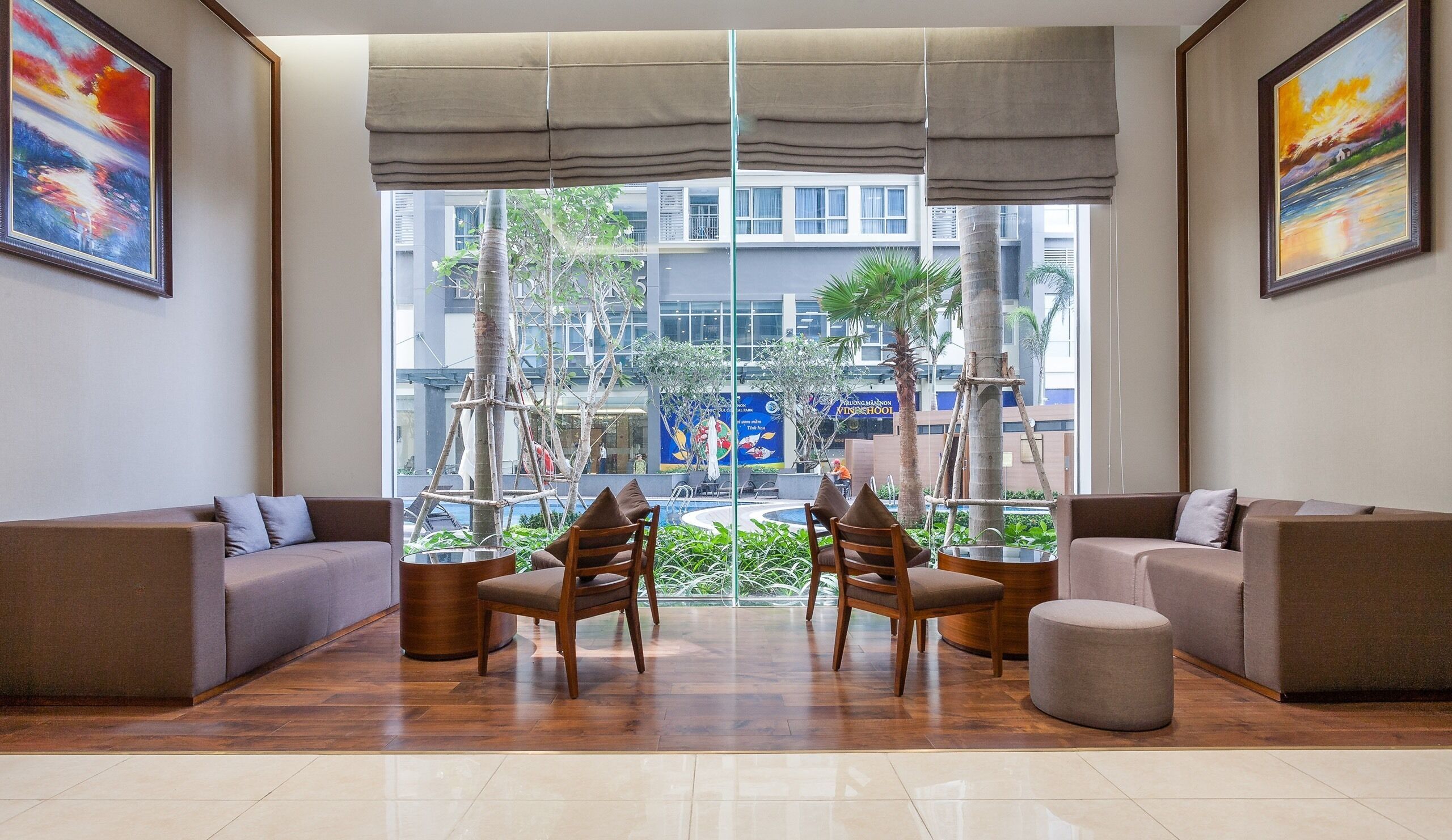 A modern lounge area with two sofas, a round table, and chairs, featuring a view of a cityscape and a pool.