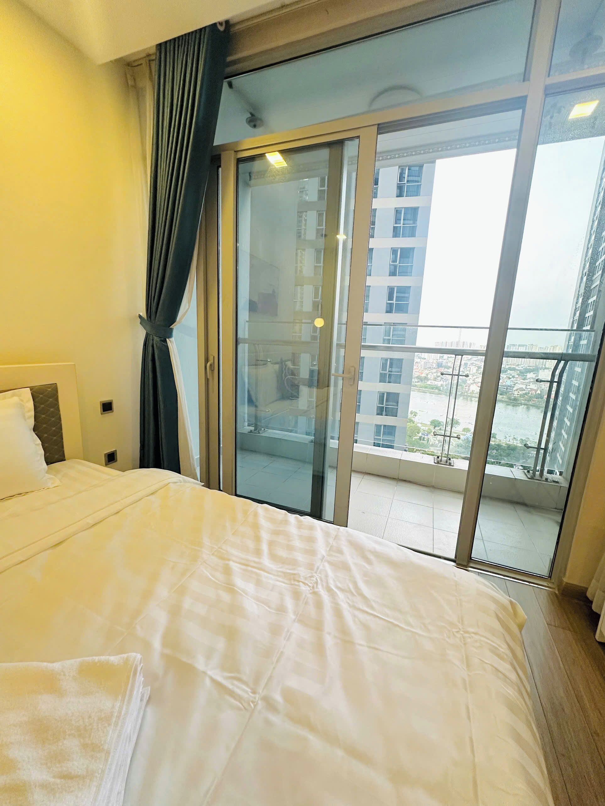 A hotel room with a large bed, a sliding glass door leading to a balcony with a city view.