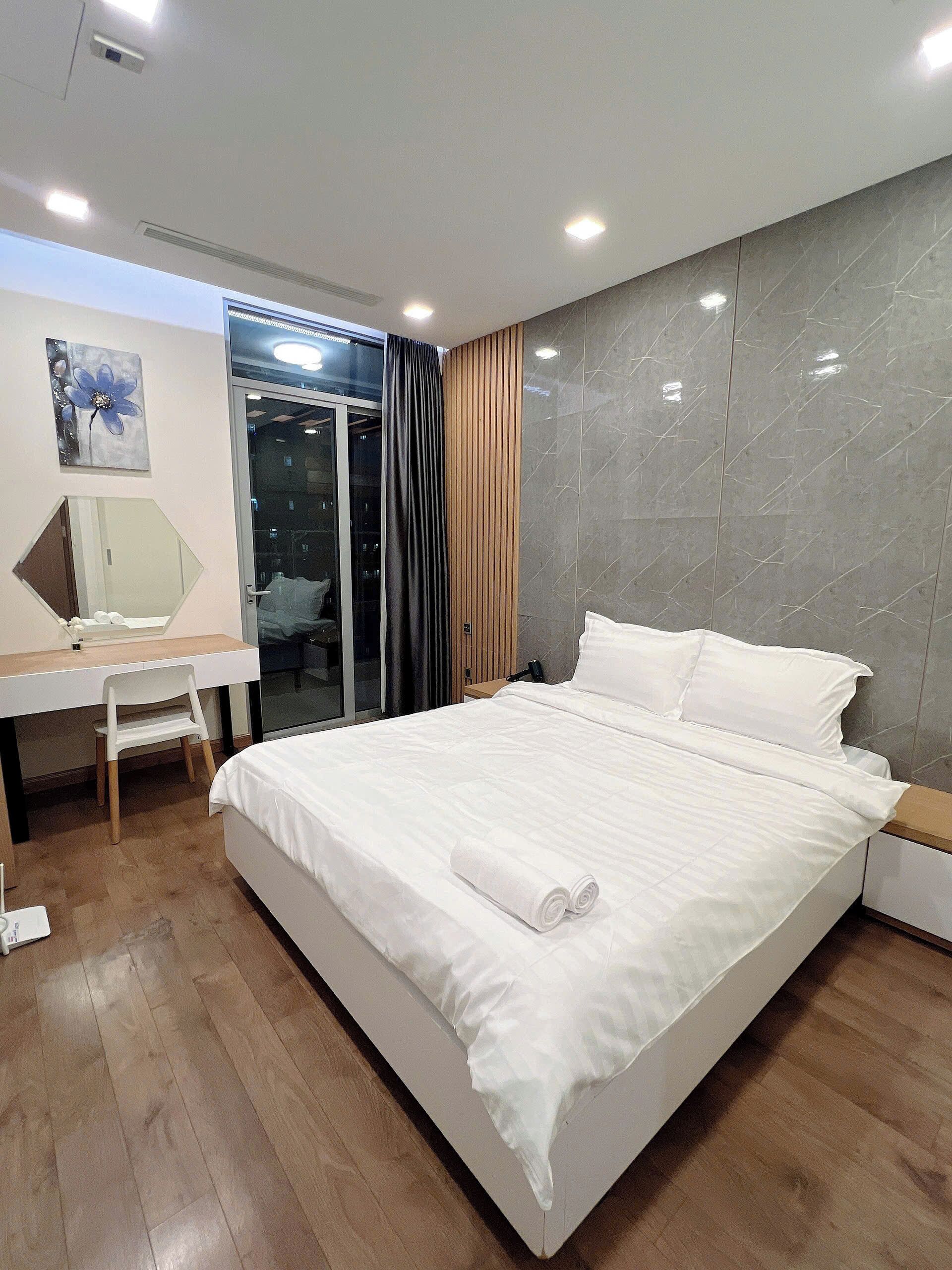 Habitación de hotel moderna con una cama grande, un escritorio con silla, un espejo y vistas a la ciudad a través de una puerta de cristal.
