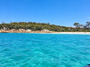 Une plage bordée d’une eau turquoise et limpide, de formations rocheuses et, en arrière-plan, d’une végétation luxuriante.