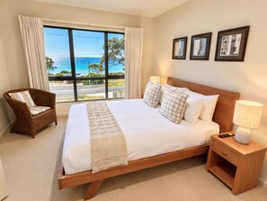 A hotel room with a large bed, a chair, a nightstand, and a view of the ocean.