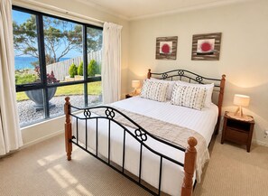 A bedroom with a large window, a bed with white bedding, two bedside tables with lamps, and artwork on the wall.