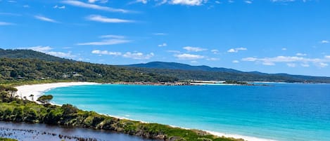A coastal landscape with a clear sky, a beach, and a road leading to the shore.