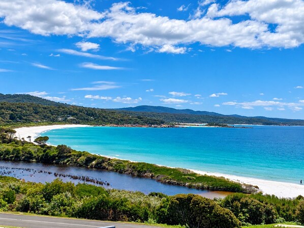A coastal landscape with a clear sky, a beach, and a road leading to the shore.