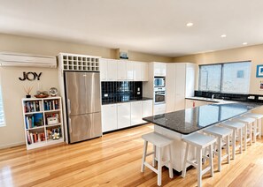 A modern kitchen with white cabinetry, a stainless steel refrigerator, a built-in oven, and a glass island with bar stools. - Lichen Villa Bay of Fires  - Binalong Bay beach is at your doorstep (Binalong Bay)