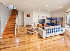 A living room with a sofa, a chair, a television, a bunk bed, and a wooden staircase. - Lichen Villa Bay of Fires  - Binalong Bay beach is at your doorstep (Binalong Bay)