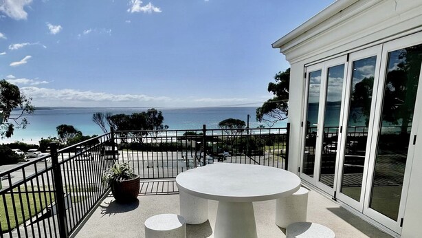 Un balcón con una mesa redonda y sillas, una planta en maceta y vista al mar.