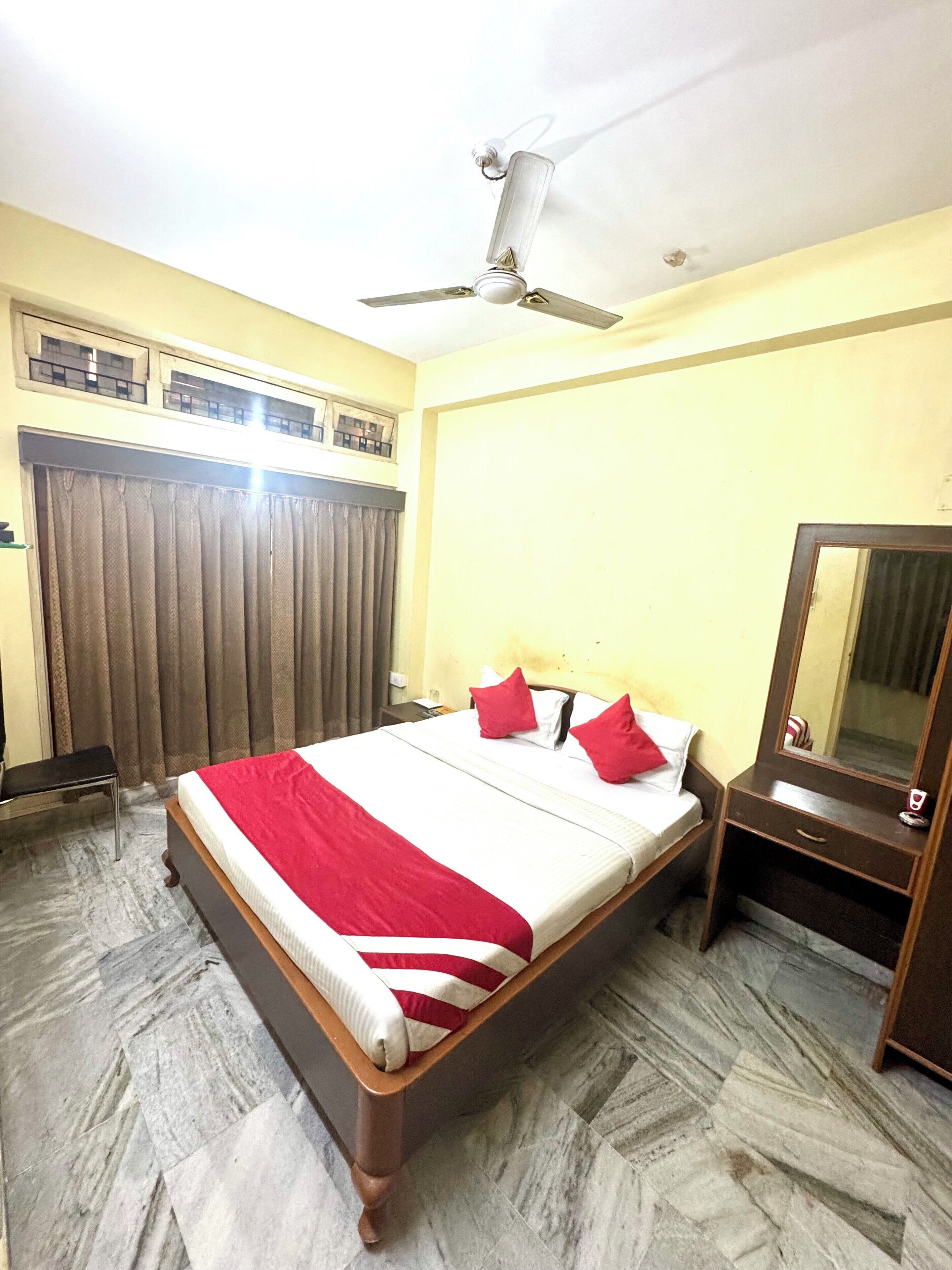A hotel room with a bed, a ceiling fan, a mirror, and a window with curtains.