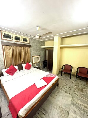 Een hotelkamer met een groot bed, een plafondventilator, een bureau, twee stoelen en een kledingkast.