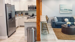 Een moderne keuken met roestvrijstalen apparatuur, een eetgedeelte met een houten tafel, en een woonkamer met een blauwe bank en een salontafel.