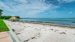 Een strand met een rieten parasol, een grasveld en een helderblauwe lucht.