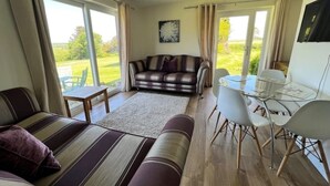 Un salón con sofá, una mesa de vidrio y sillas. Se ve una ventana con vistas a follaje exterior.