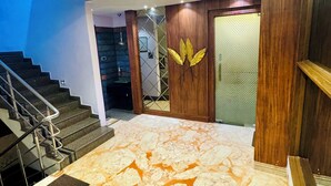 A modern interior with a marble floor, a staircase, and a wooden door with a golden leaf design. - Onyx Garden Boutique Hotel (Guwahati)