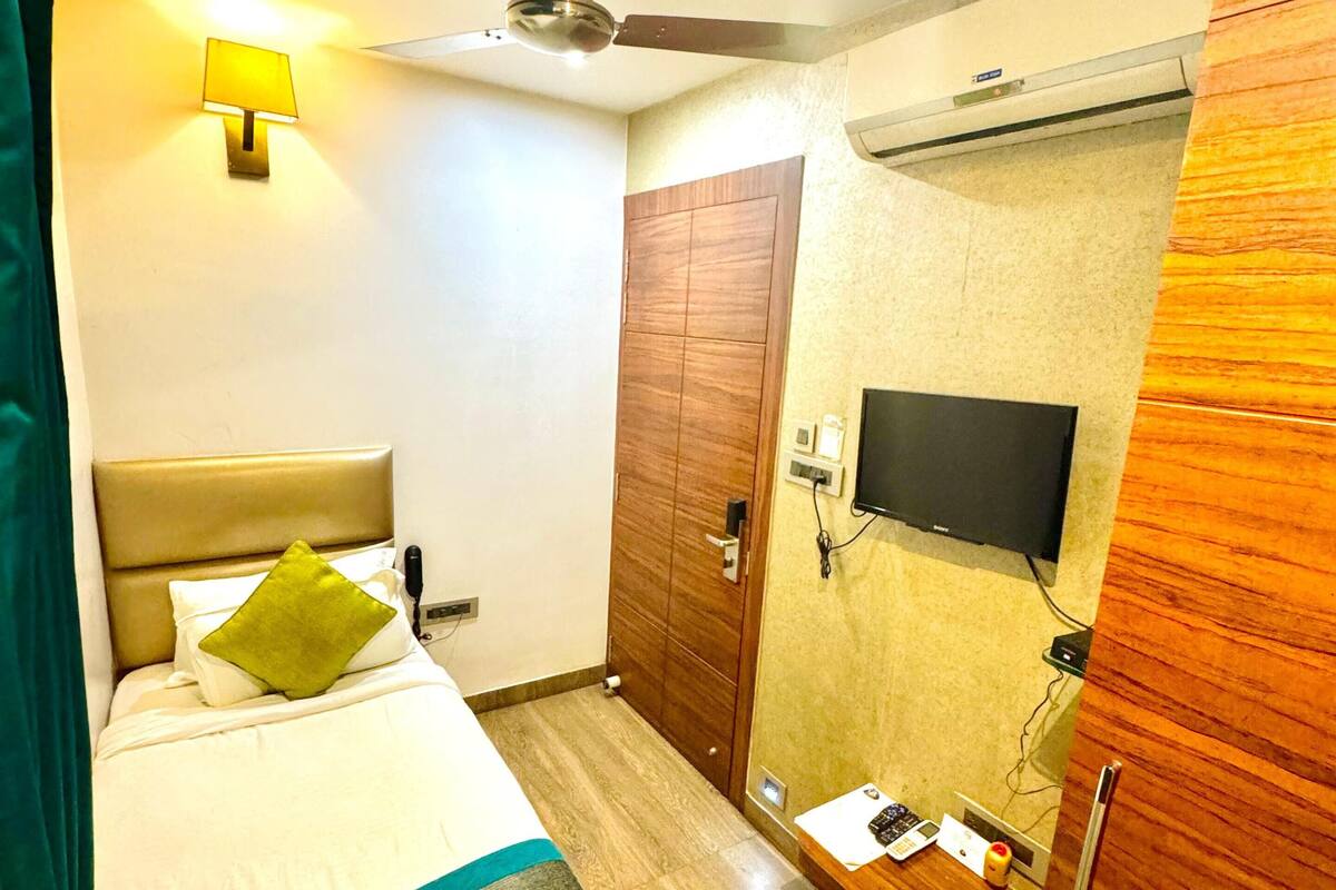 A hotel room with a bed, a ceiling fan, a TV mounted on the wall, and a wardrobe.
