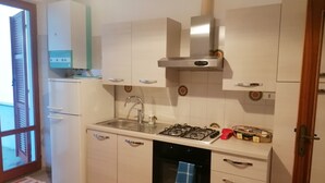 A compact kitchen with a gas stove, sink, and a built-in oven. There is a refrigerator to the left and a window with blinds. - Apartment 1st row sea with beautiful terrace (Grottammare)
