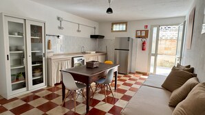 Una cocina compacta con refrigerador, pileta y armarios. Hay una mesa de comedor con sillas y un sofá con cojines. El piso tiene un diseño de cuadros.