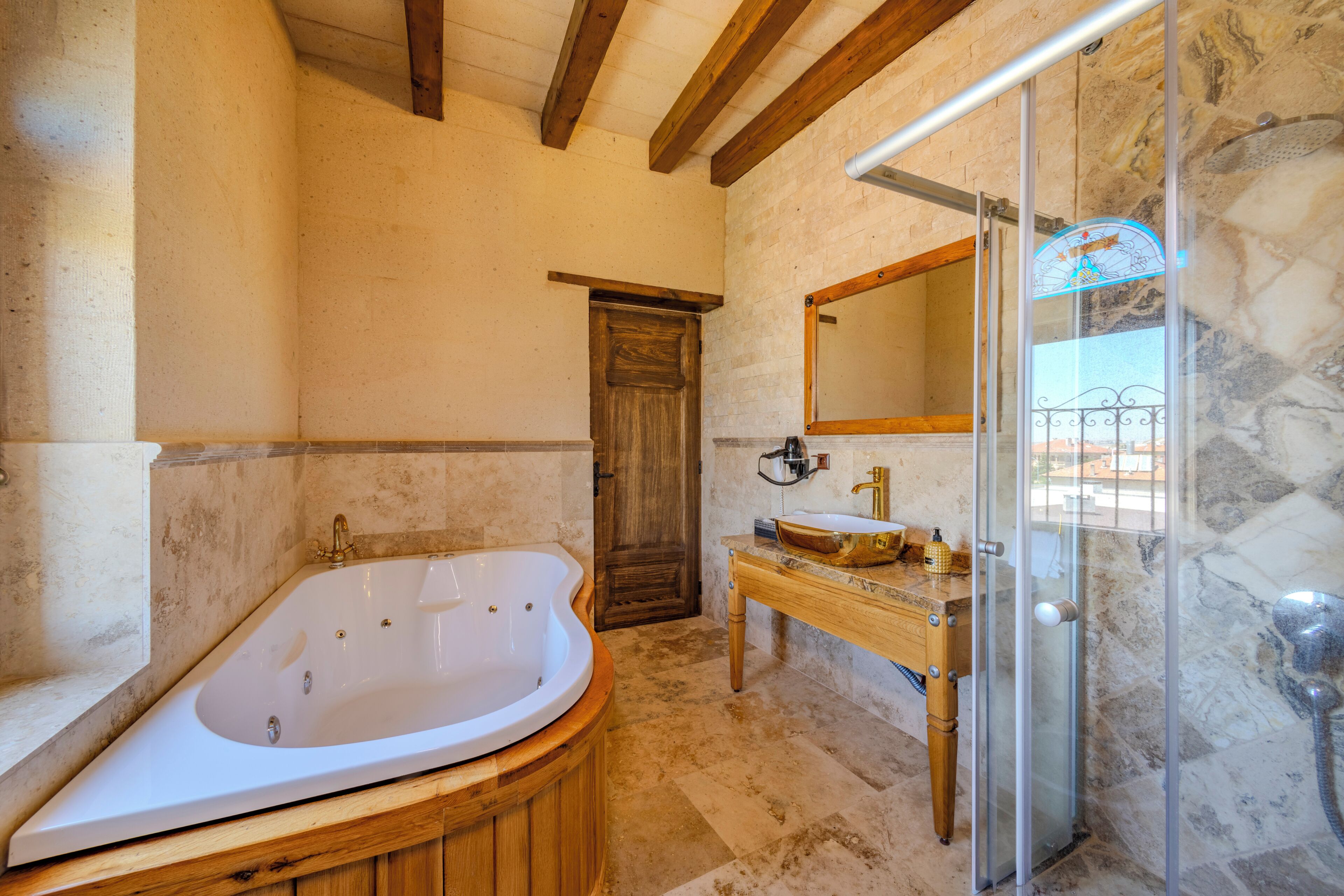 A bathroom with a freestanding bathtub, a wooden vanity, a glass shower enclosure, and a stone wall.