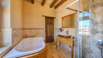 A bathroom with a freestanding bathtub, a wooden vanity, a glass shower enclosure, and a stone wall.