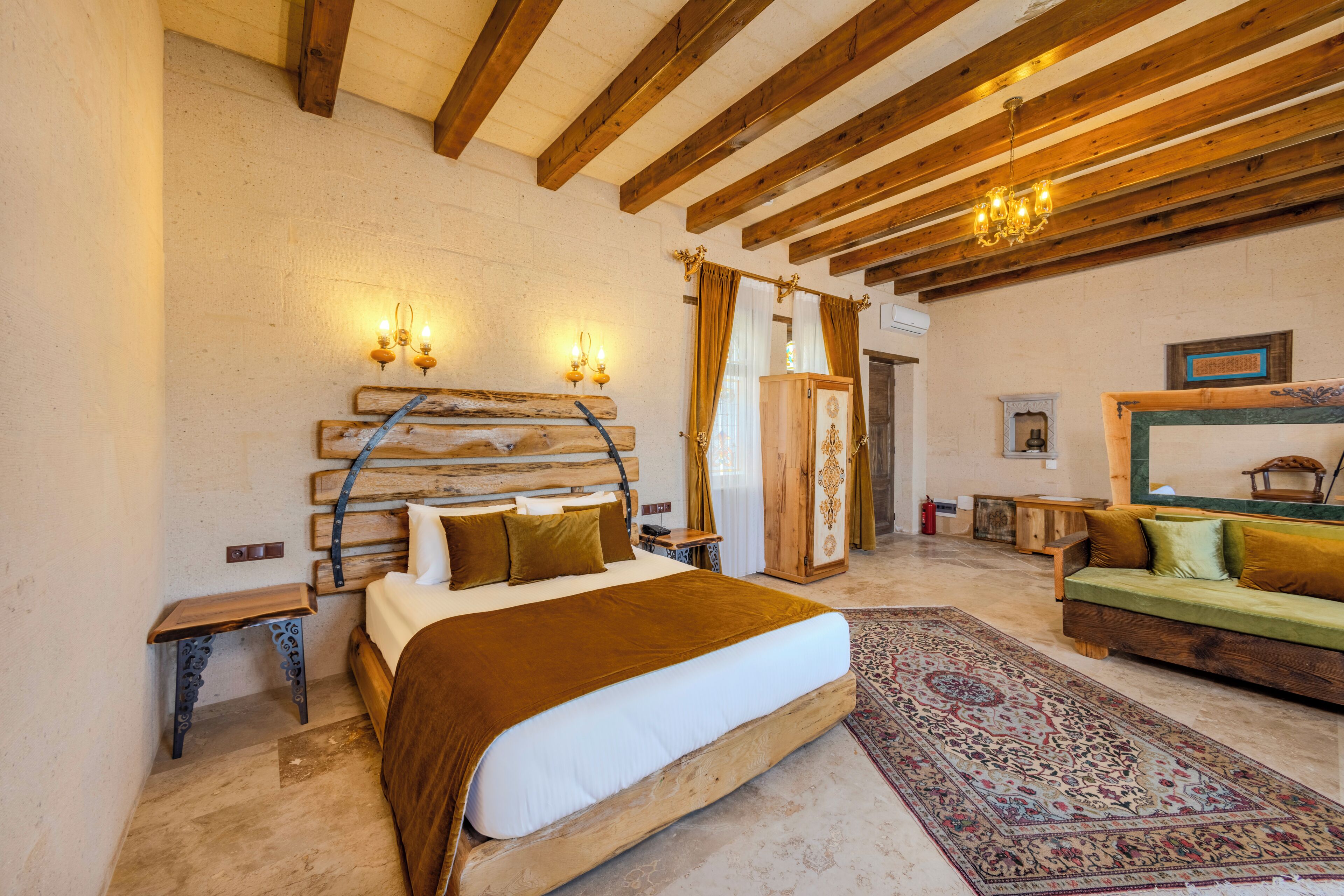Un dormitorio con una cama de madera, un sofá verde, un tapiz estampado y un techo de madera con vigas a la vista.