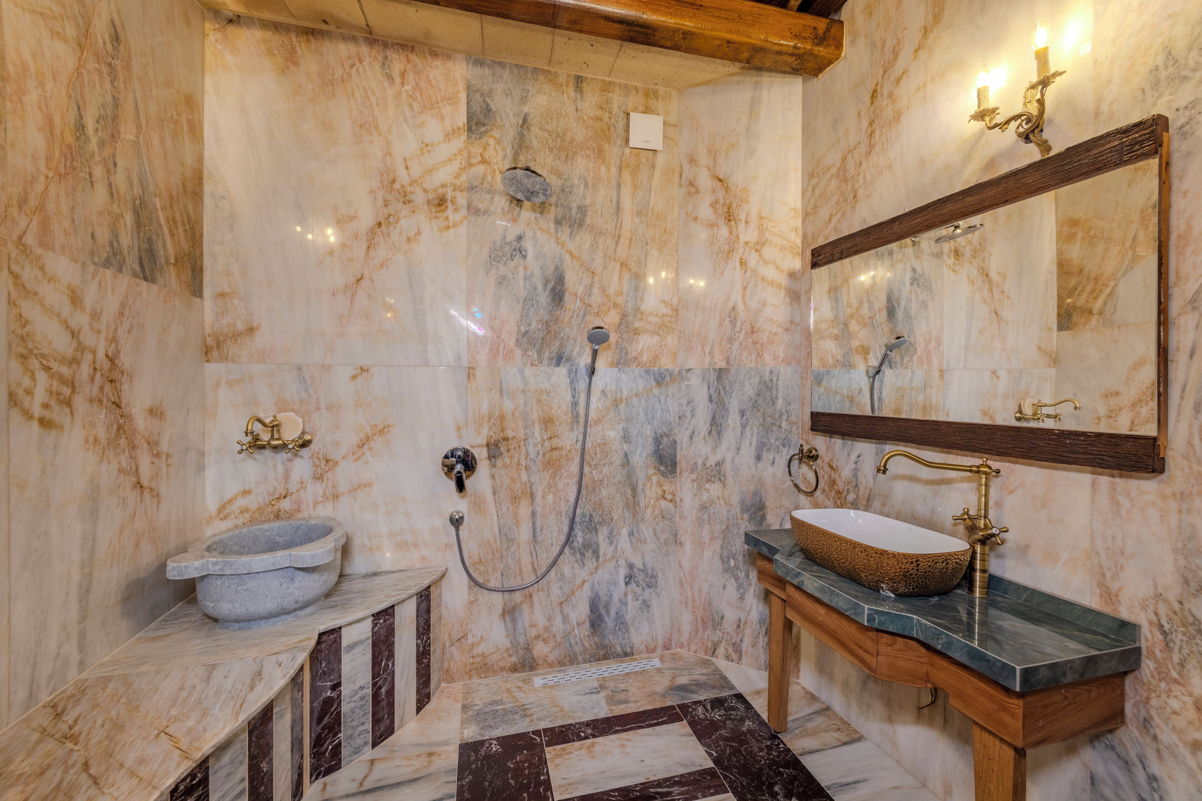 Un baño con pared de mármol, lavabo de piedra, tocador de madera y espejo.