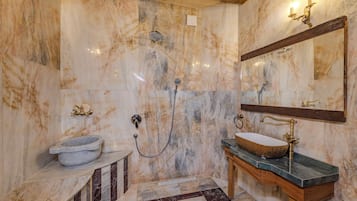 Un baño con pared de mármol, lavabo de piedra, tocador de madera y espejo.